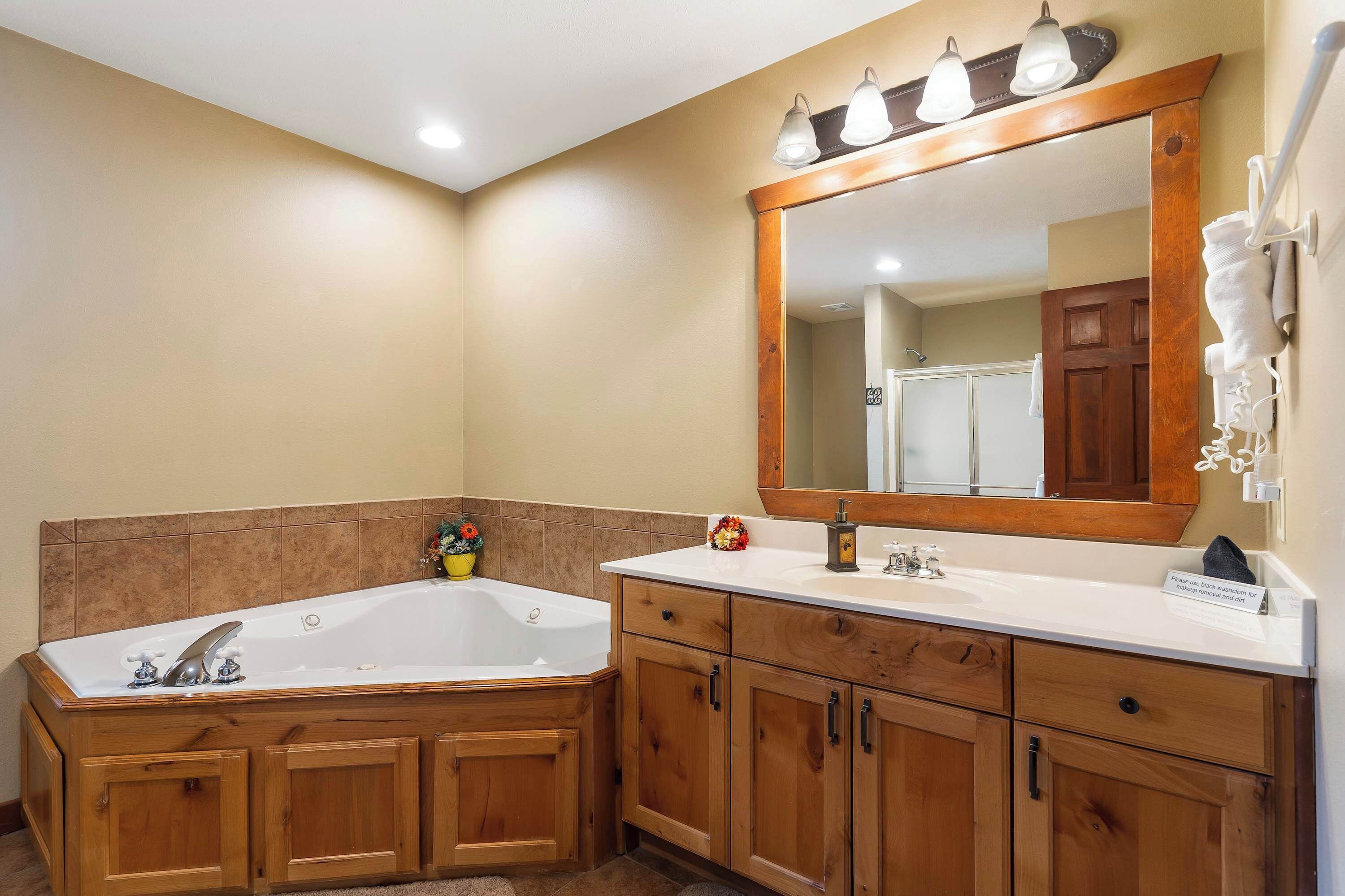 Un baño con una bañera grande, armarios de madera, un lavabo blanco y un espejo con luces.