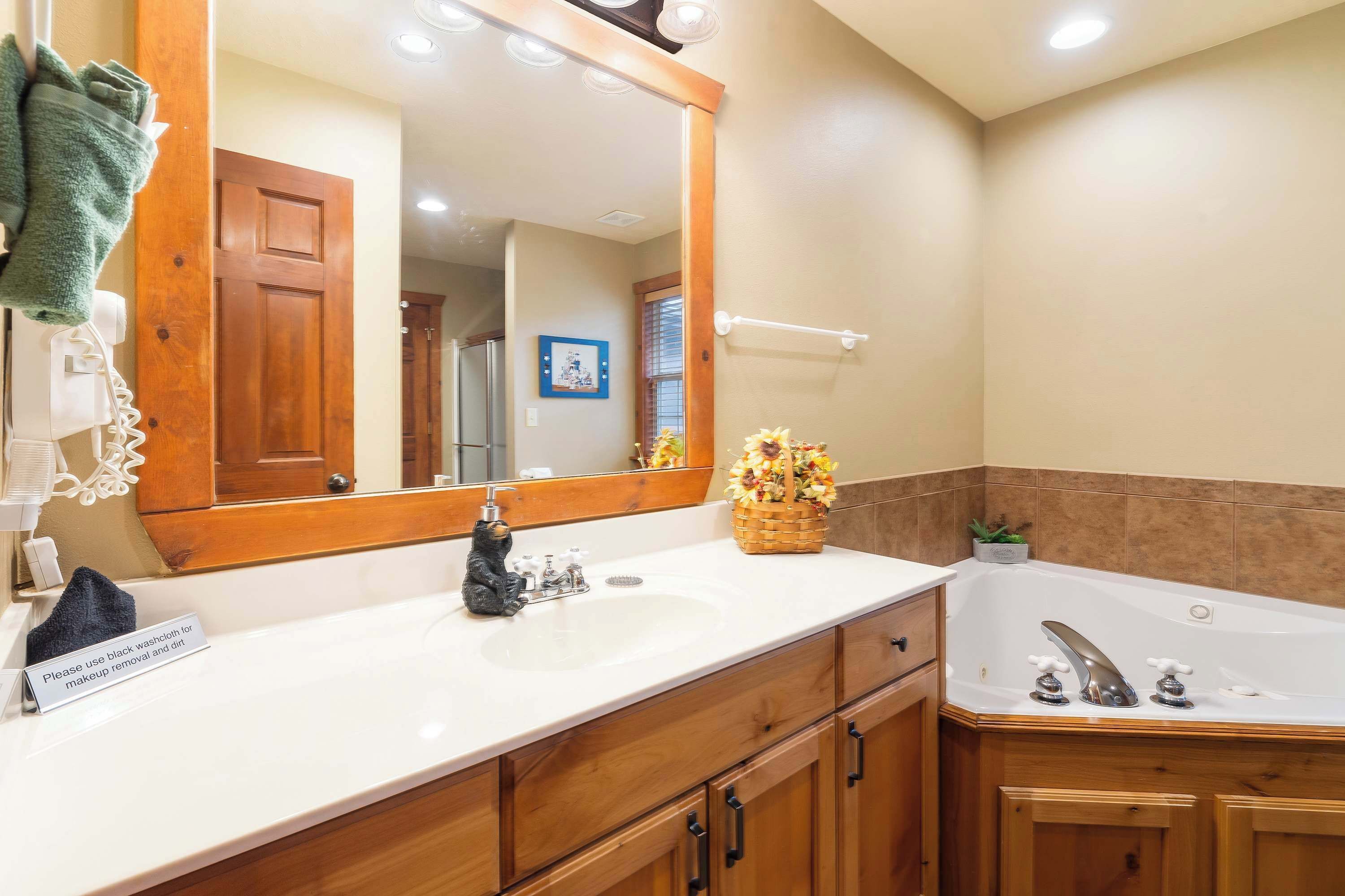 A bathroom with a large mirror, a sink, a bathtub, and wooden cabinets.