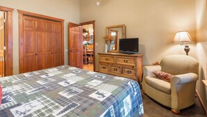 A bedroom with a large bed, a wooden dresser, a television, and a chair. - Creekside - 2 BDR Resort Cabin in Epic Location! (Branson West)