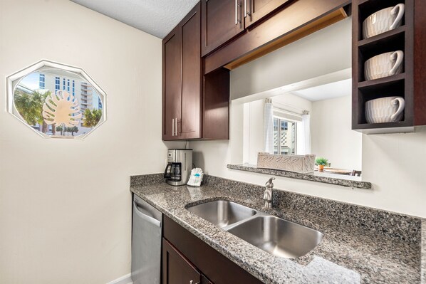 A kitchen with granite countertops, stainless steel sink, and dark wooden cabinets.