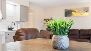 A living room with a wooden coffee table, a white textured vase with green plants, a brown leather sofa, and a kitchen in the background. - Chandlers Pondview Getaway Chic Branson Escape (Branson)