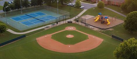 Un campo de béisbol con canchas de tenis y un parque infantil.