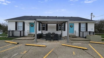 A building with a covered outdoor seating area, a blue door, and a fenced parking lot.