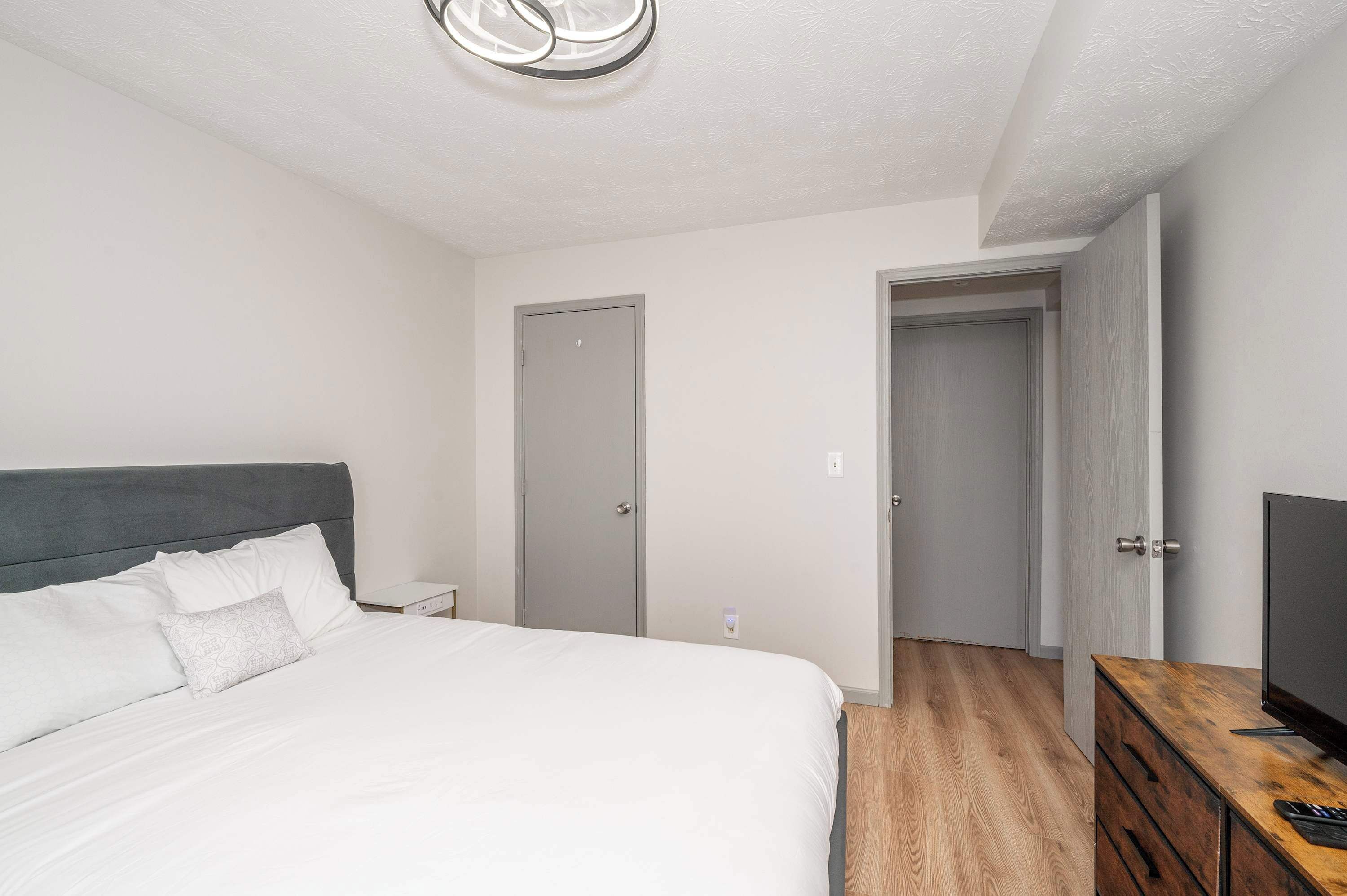 A bedroom with a bed, a TV on a wooden dresser, and two doors.
