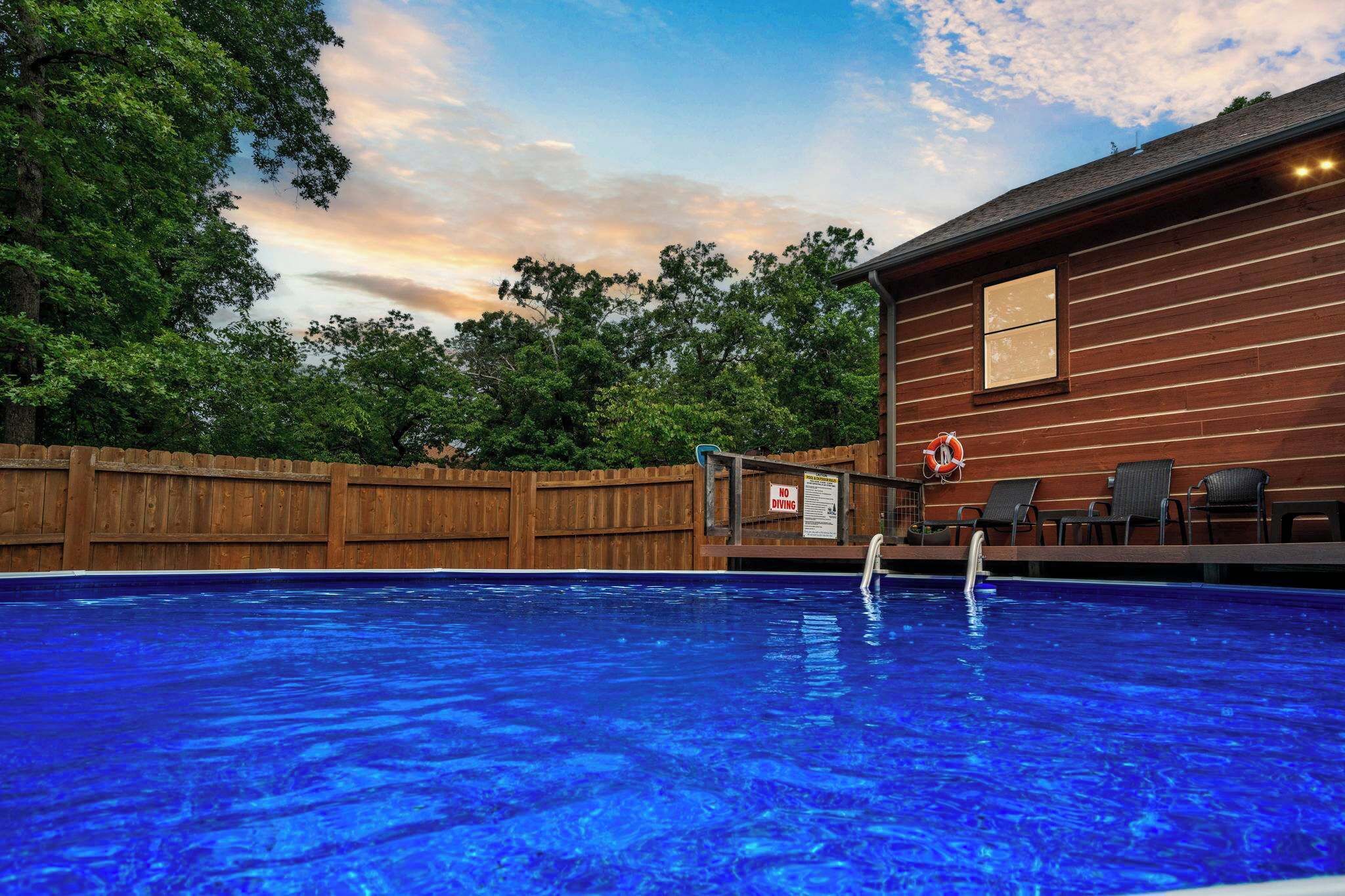 A swimming pool with a wooden deck, a lifeguard chair, and a no diving sign.