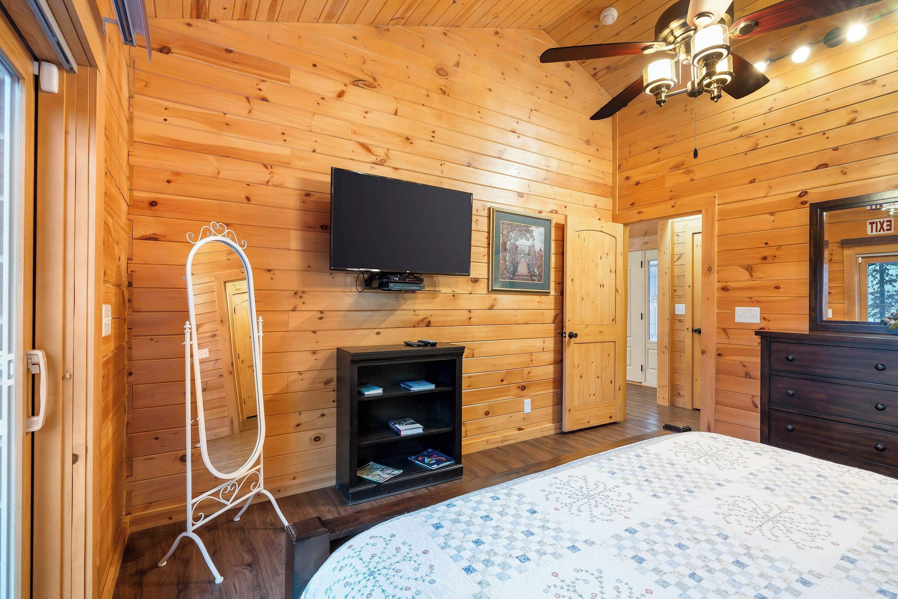 Una habitación con paneles de madera, una cama, un televisor, un espejo y una puerta señalizada con 