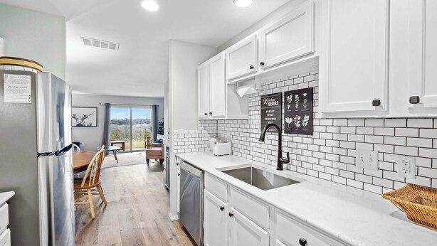 A modern kitchen with white cabinets, a stainless steel refrigerator, a dishwasher, and a black backsplash with herb labels.