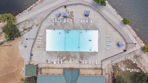 Vista aérea de un área de piscina con múltiples sillones de descanso y sombrillas.