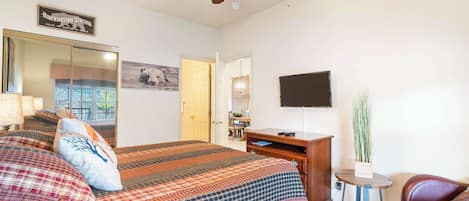 A bedroom with a large bed, a ceiling fan, a TV, a desk, and a chair.