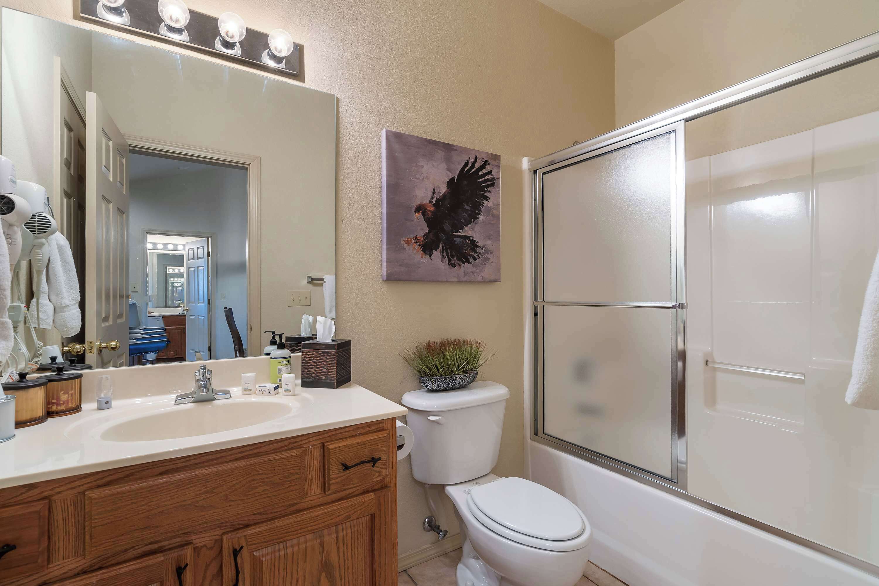 A bathroom with a white sink, wooden vanity, a toilet, a shower with a glass door, and a wall-mounted light fixture.