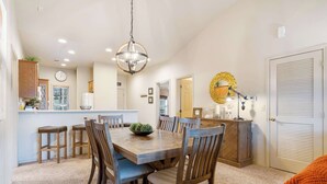 Un comedor con una mesa y sillas de madera, una araña y una cocina al fondo.