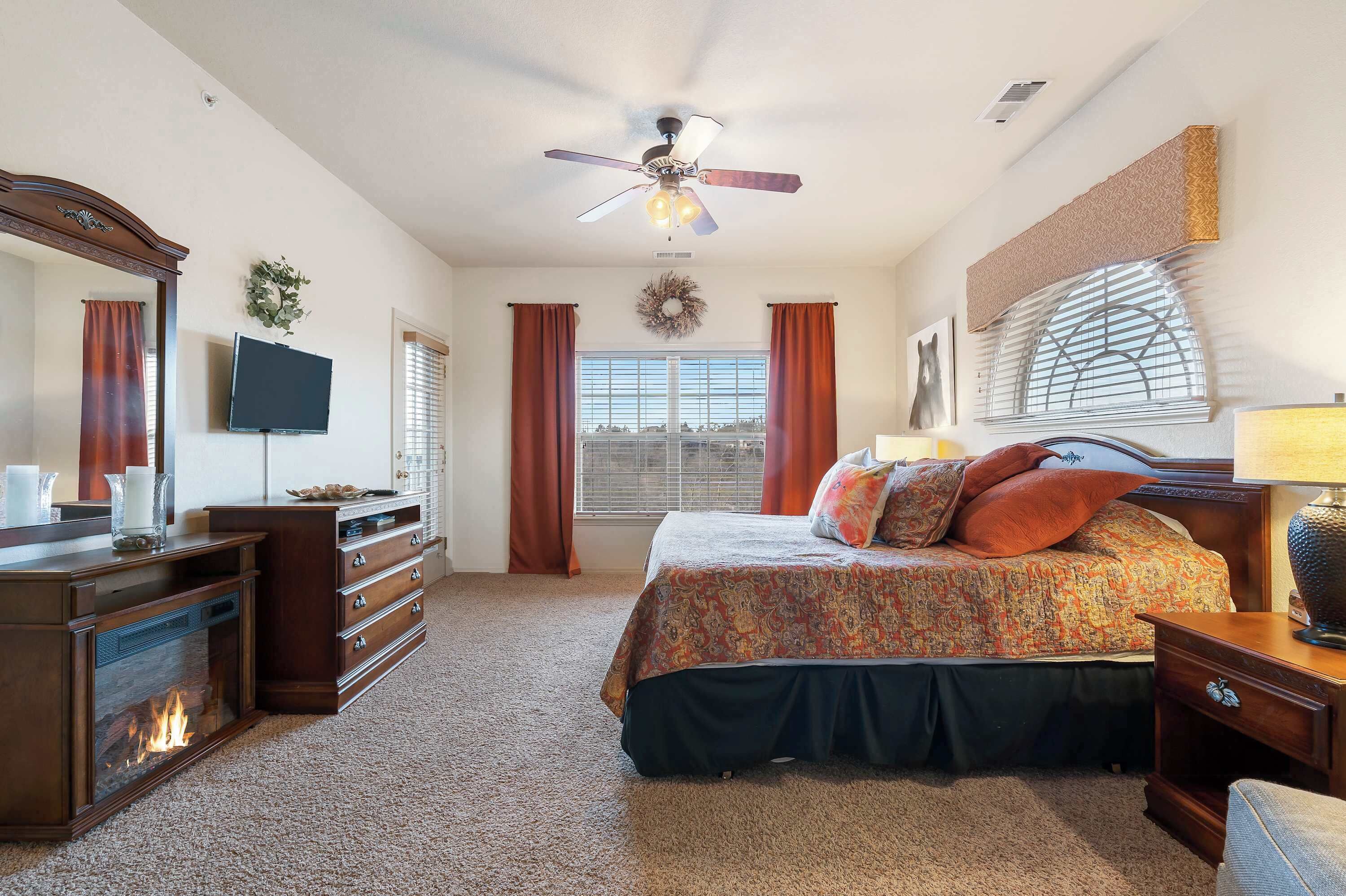 A bedroom with a bed, dresser, TV, fireplace, and a ceiling fan.