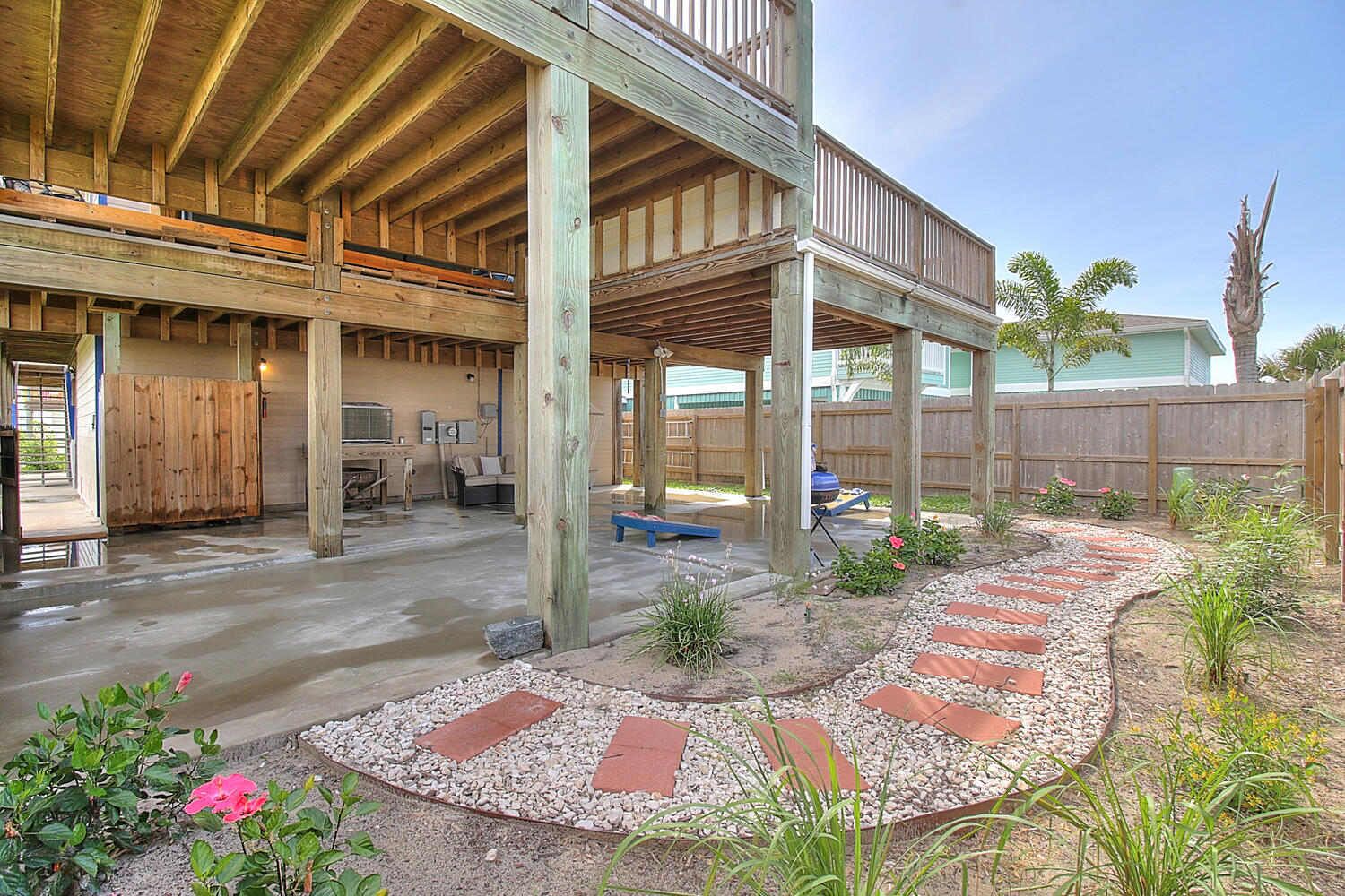 Um deck aberto com piso de madeira, cercado por um jardim com caminho de pedras e plantas.