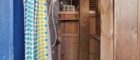 A wooden shed with a white plastic container on top, a blue wall with a white door, and a polka dot curtain.