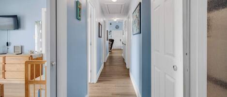 A hallway with wooden flooring, white doors, and a television on the left wall.
