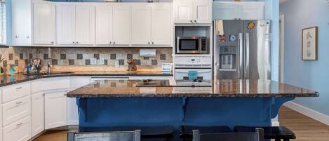 A kitchen with white cabinets, a blue island, and a stainless steel refrigerator.