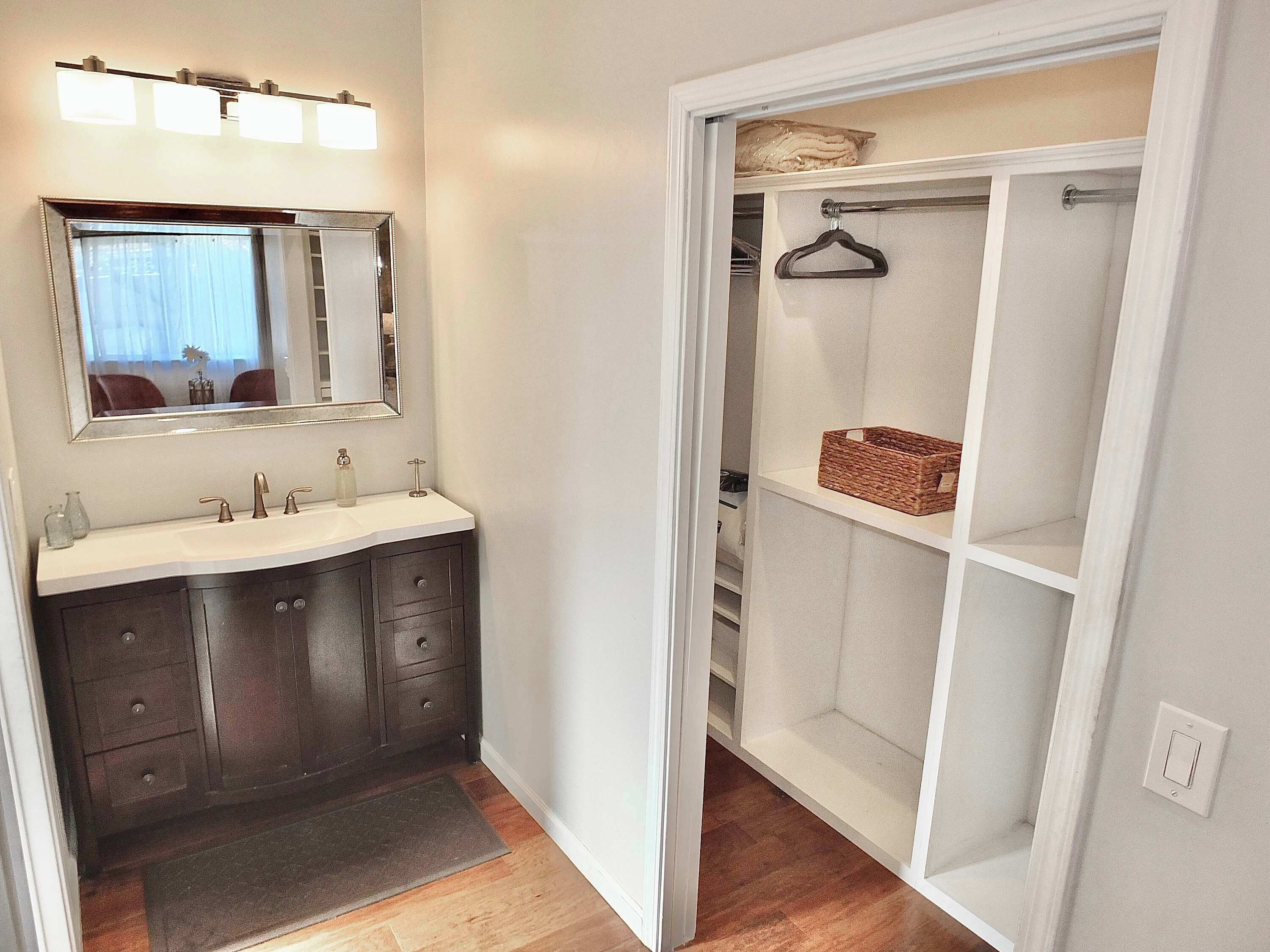 Un baño con tocador, espejo y un vestidor con estantes y barra para colgar.