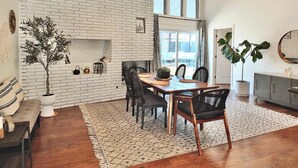 A dining area with a brick wall, wooden table, chairs, and a large potted plant. - Bellflower Breeze Charming 3 BDR in Long Beach! (Long Beach)