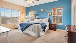 A bedroom with a bed, two windows with blinds, a ceiling fan, and a dresser.