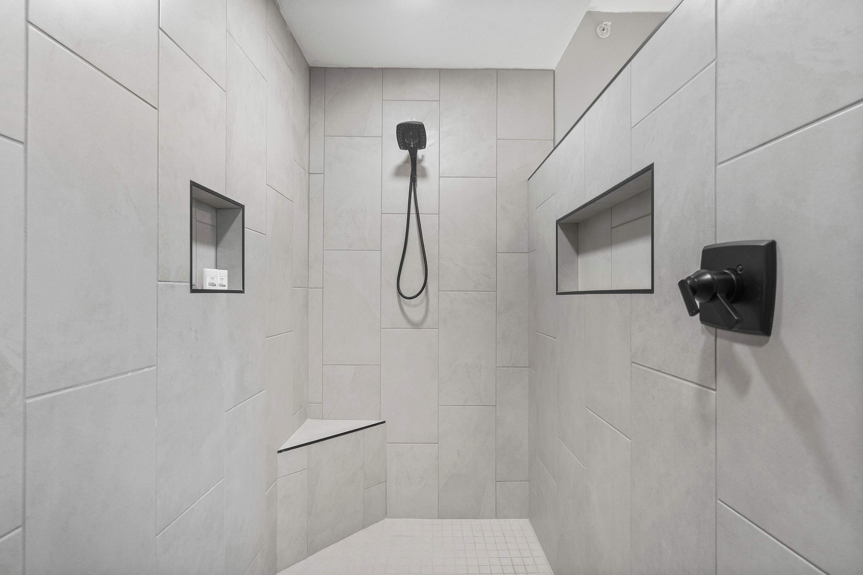 Una ducha moderna con cabezal de ducha de mano, panel de control en la pared y un espejo pequeño.