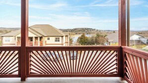 A covered outdoor area with a wooden railing, a view of houses and a lake in the background.