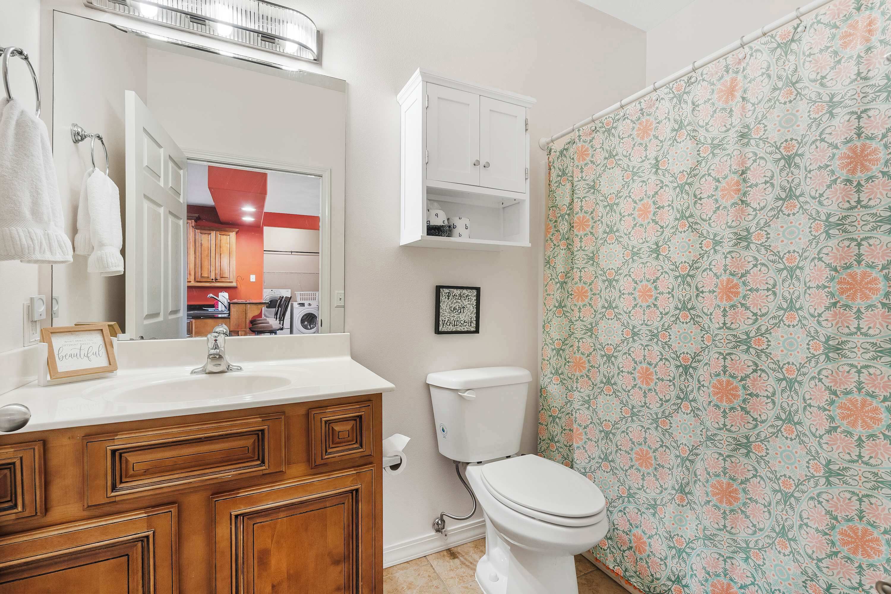 A bathroom with a white sink, wooden vanity, a toilet, and a shower curtain with a floral pattern.