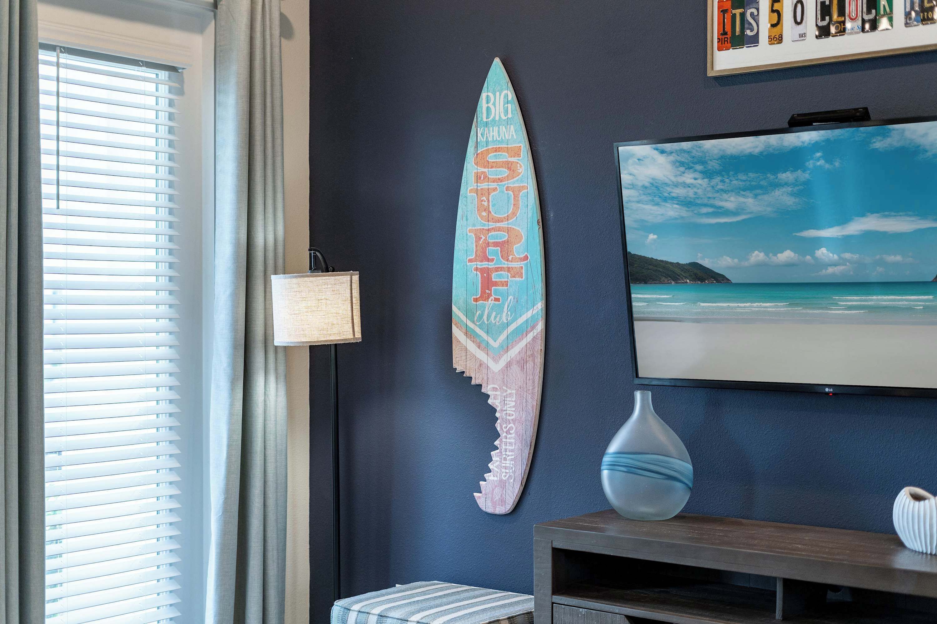 A room with a surfboard decoration, a television, and a vase on a shelf.