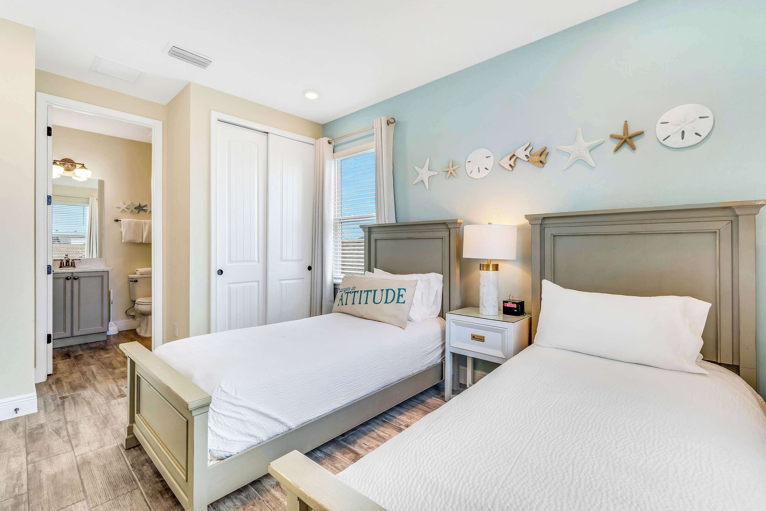 A bedroom with two beds, a nightstand, a dresser, and a bathroom visible through an open door.