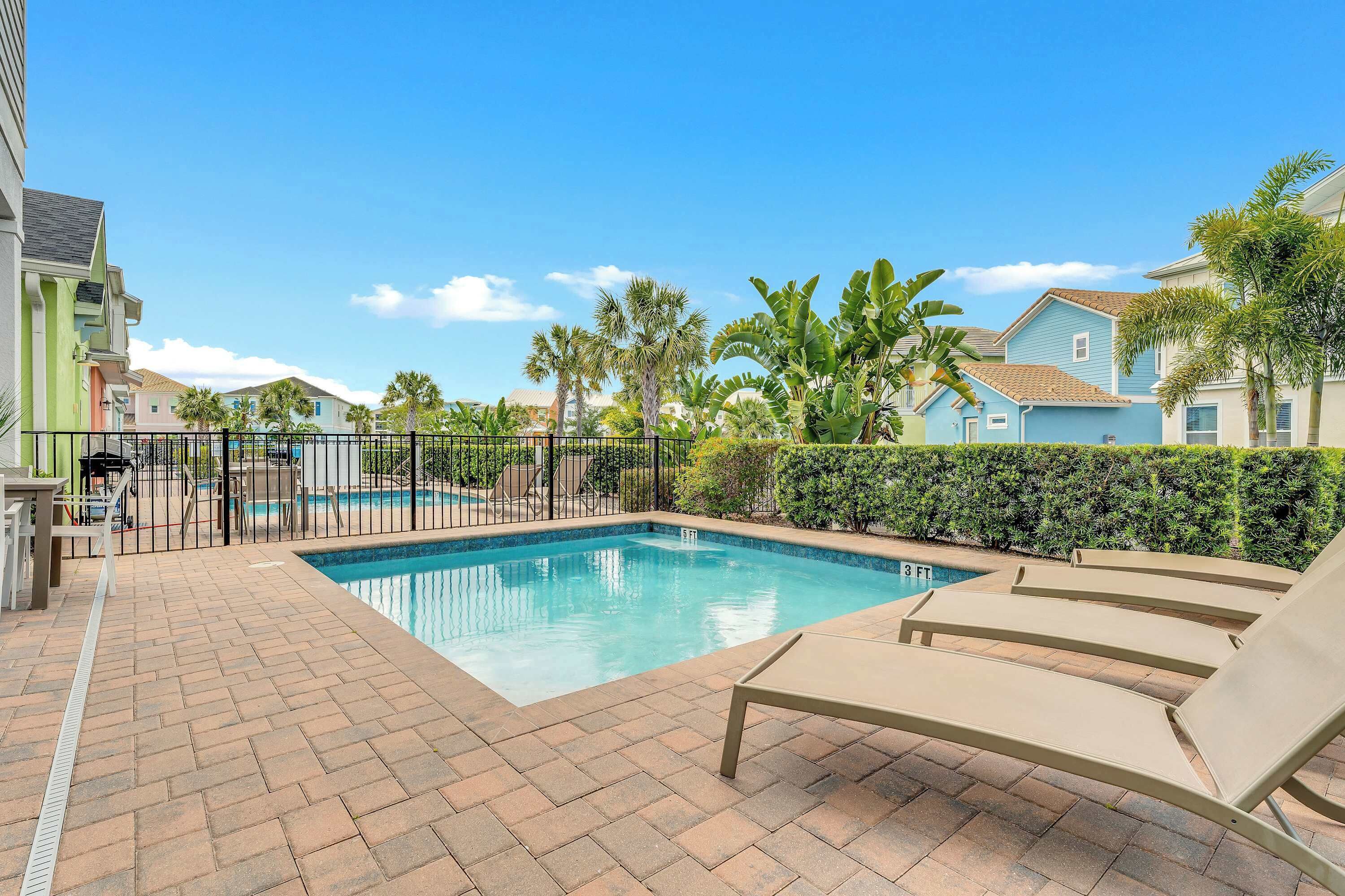 A swimming pool with lounge chairs, a brick patio, and a fence.