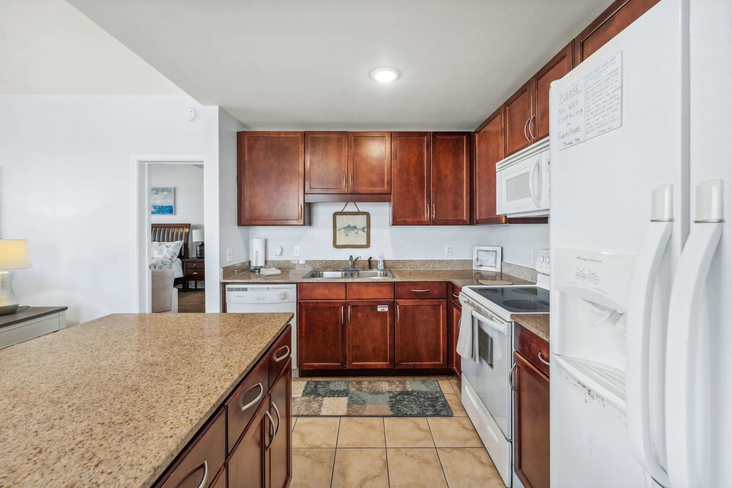 A kitchen with wooden cabinets, a granite countertop, a microwave, a stove, and a refrigerator.