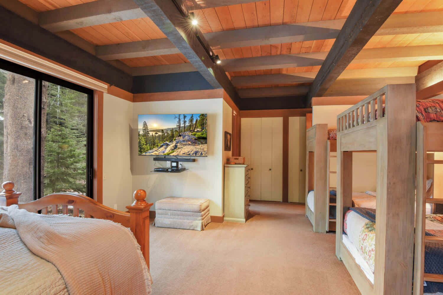 Une chambre avec un lit superposé en bois, un téléviseur fixé au mur et une fenêtre donnant sur les arbres.