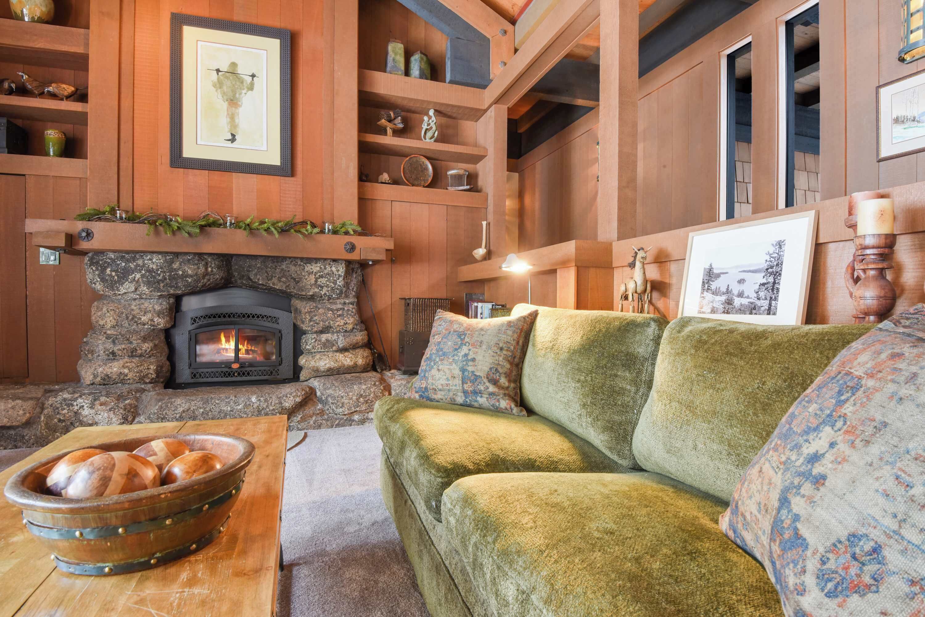 Un salon chaleureux avec une cheminée en pierre, des étagères en bois et un canapé vert.