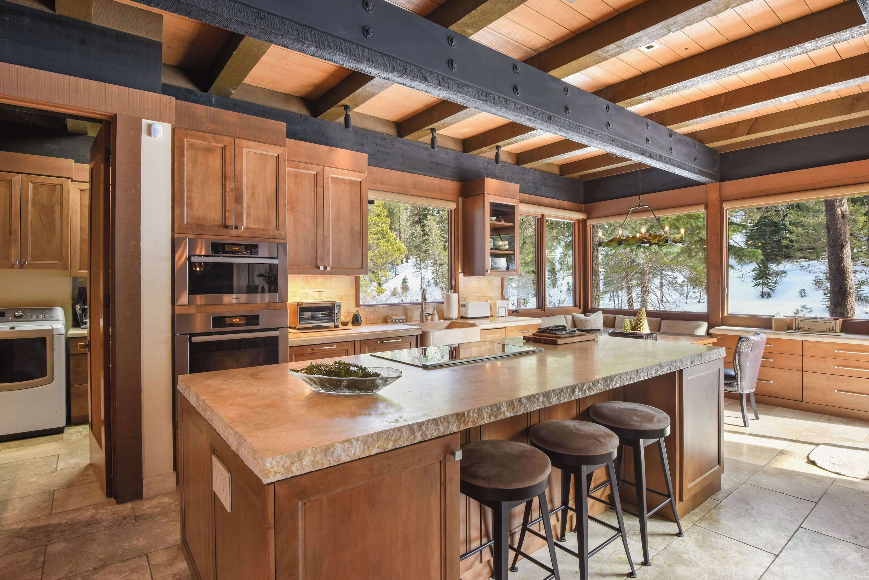 A spacious kitchen with wooden cabinets, a large island with stools, and a view of a lake.