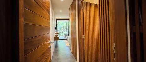 A hallway with wooden paneling and a stone floor leading to a room with a view of trees.