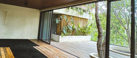 A modern interior with a wooden floor, large sliding glass doors leading to a balcony with plants and a tree.