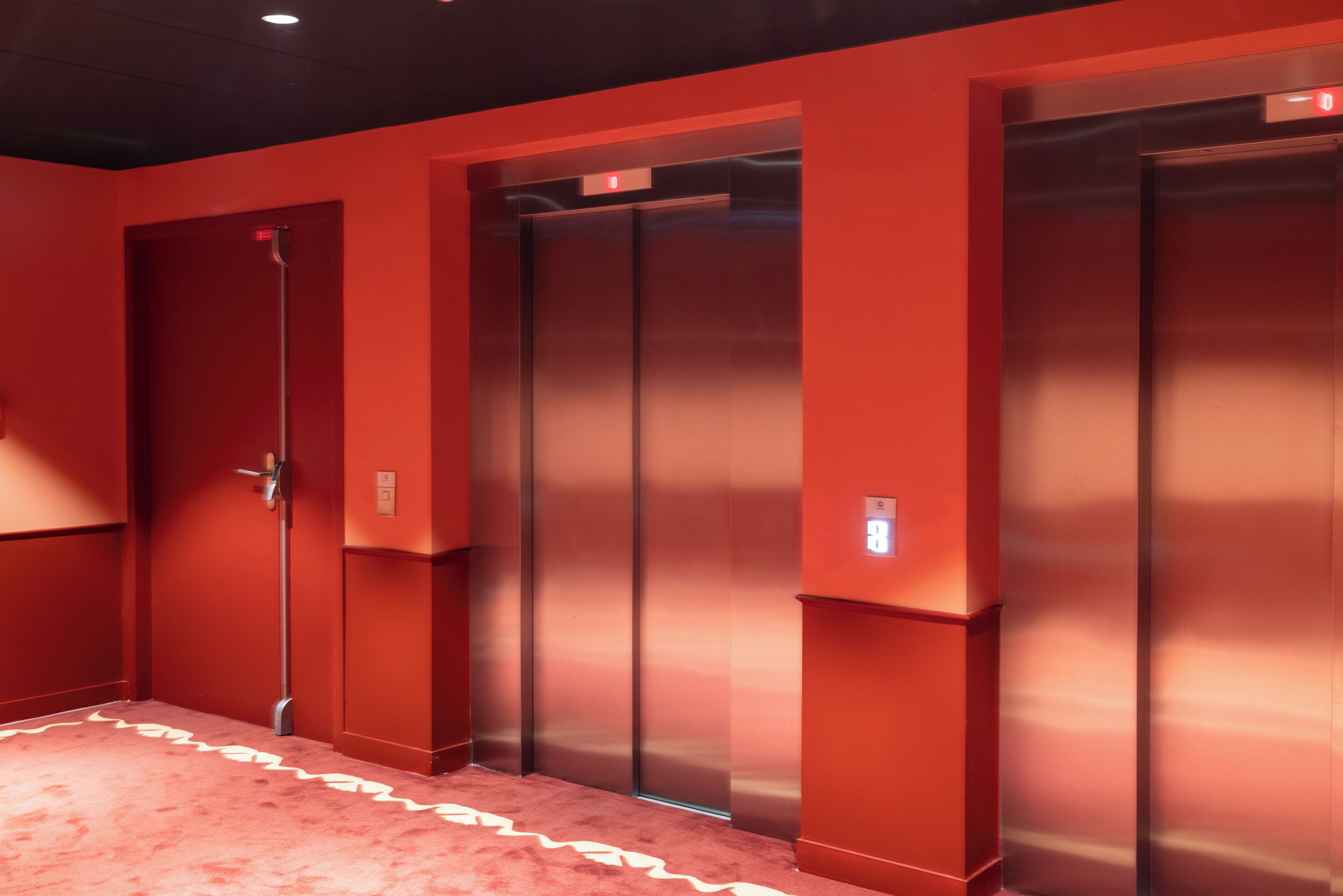 A hallway with red walls and a carpet with a white zigzag pattern.