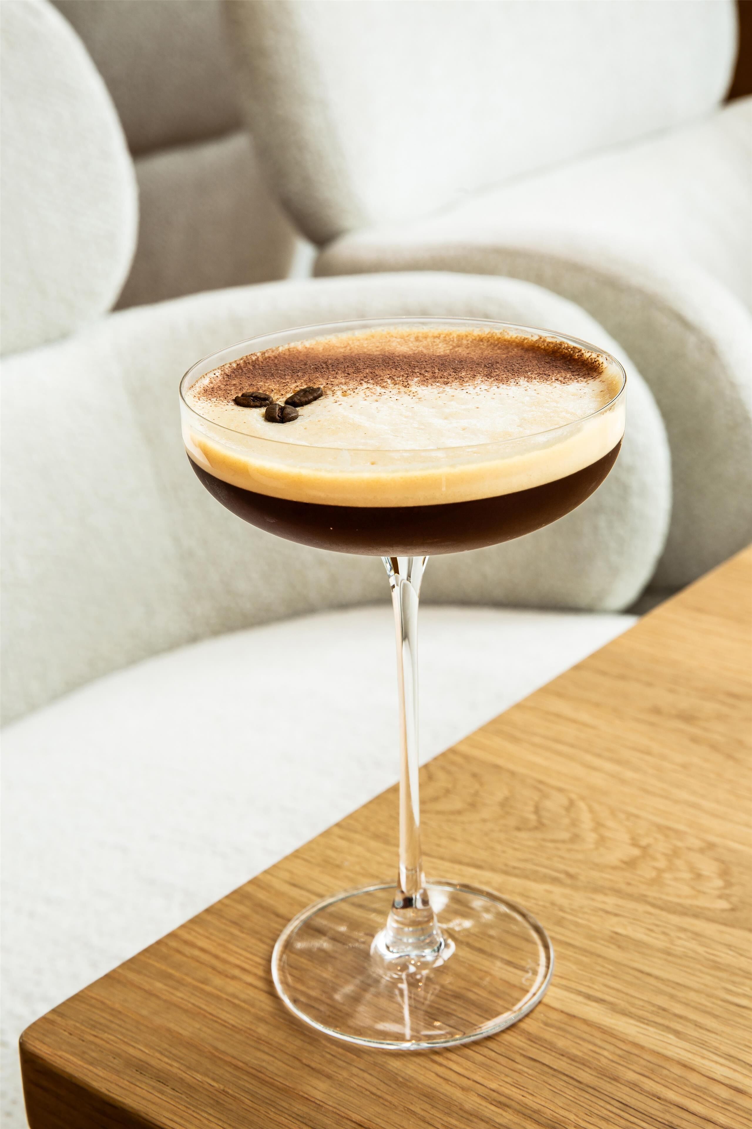 A cocktail in a stemmed glass on a wooden table with a sofa in the background.
