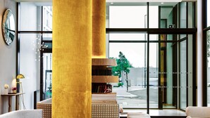 Een moderne lobby met een grote gouden zuil, zithoek en uitzicht door grote ramen.