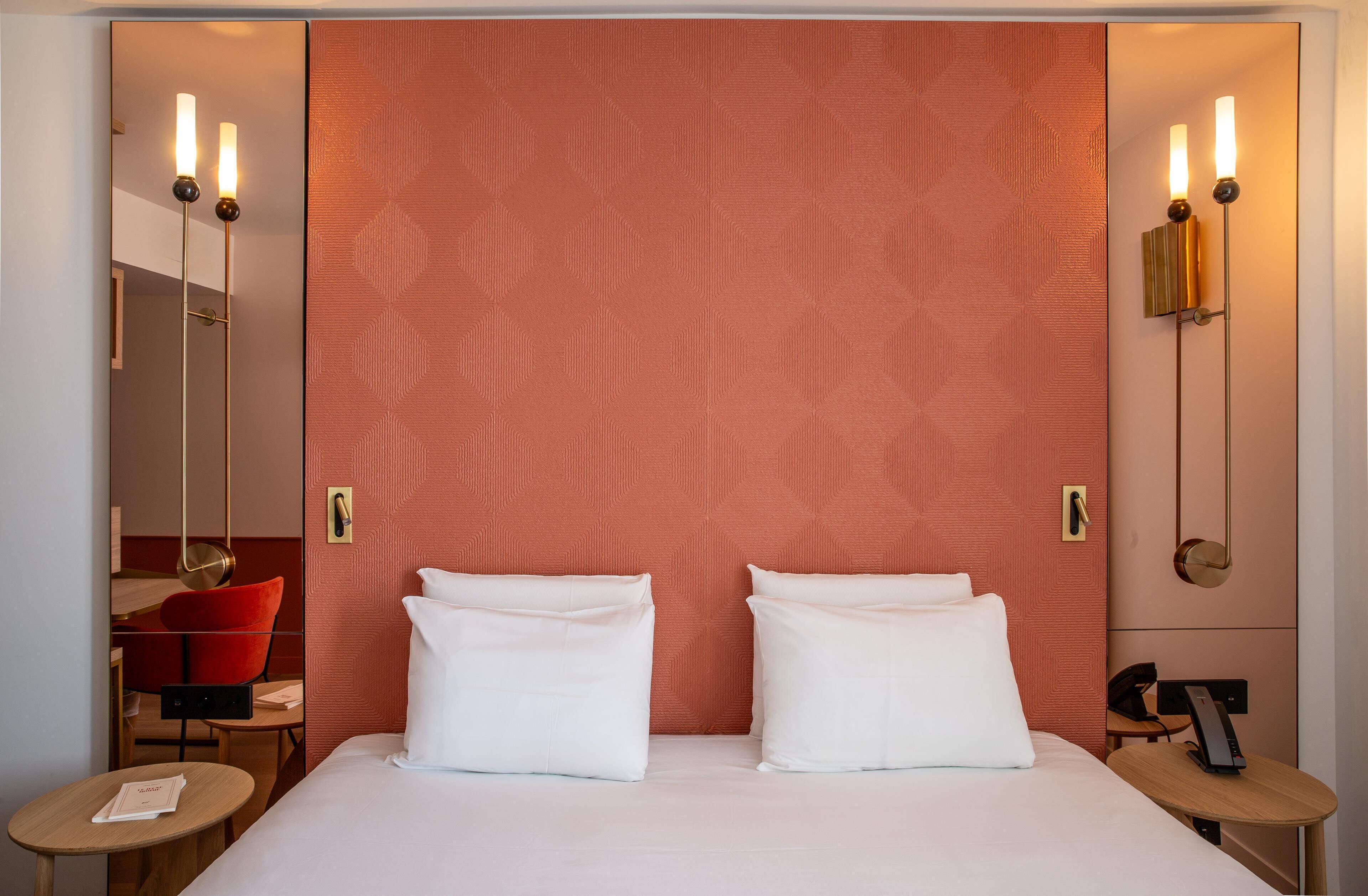 A hotel room with a large bed, two bedside tables, a red patterned headboard, and a red chair.