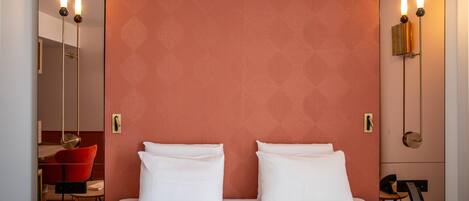 A hotel room with a large bed, two bedside tables, a red patterned headboard, and a red chair.