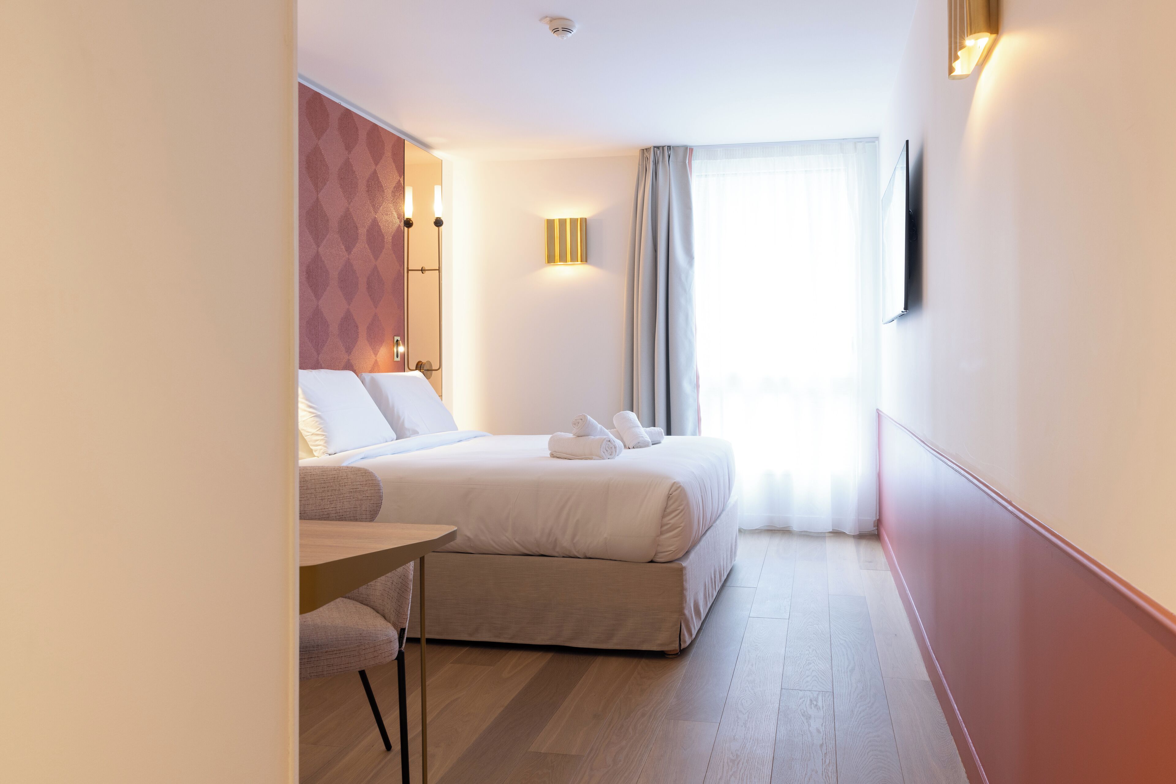 Une chambre d’hôtel moderne équipée d’un lit, d’un bureau et d’un téléviseur fixé au mur.