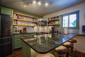 A modern kitchen with green cabinets, a large island with stools, a microwave, and various kitchen appliances. - Mtn Modern Couples Retreat PetFriendly;FencedYard;Lake;Beach;Pool;JimThorpe;Ski (Albrightsville)