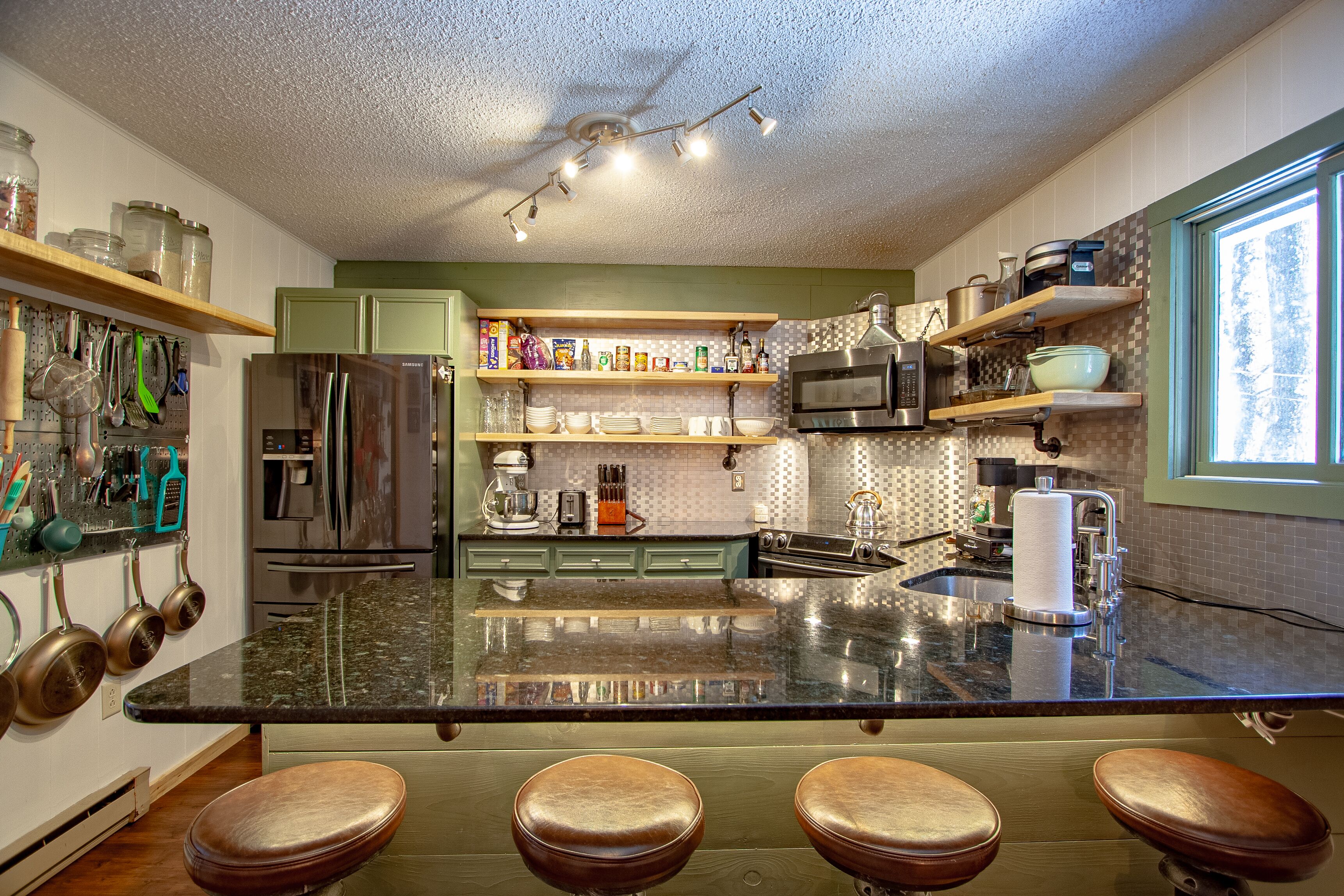 A modern kitchen with a central island, stainless steel appliances, and bar stools.