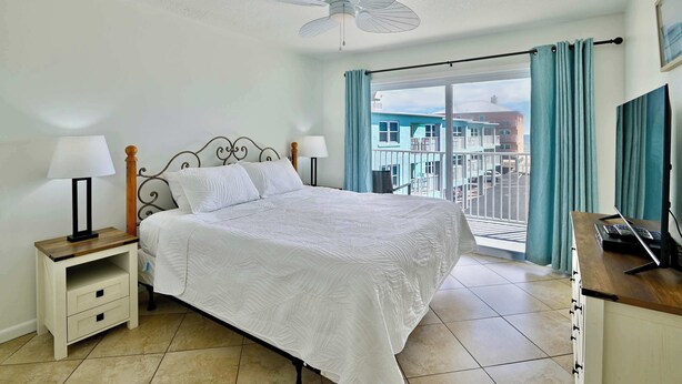 A bedroom with a bed, bedside tables, a ceiling fan, a desk, and a window with curtains. - The Hideaway A Gulf Shores Dream Vacation! (Gulf Shores)
