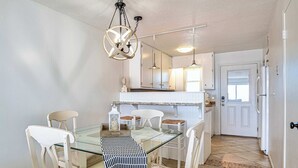 A dining area with a glass table, white chairs, and a hanging light fixture. - The Hideaway A Gulf Shores Dream Vacation! (Gulf Shores)
