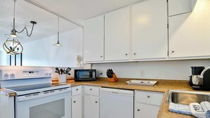 A modern kitchen with white cabinetry, a built-in oven, a dishwasher, a microwave, and a coffee maker. - The Hideaway A Gulf Shores Dream Vacation! (Gulf Shores)