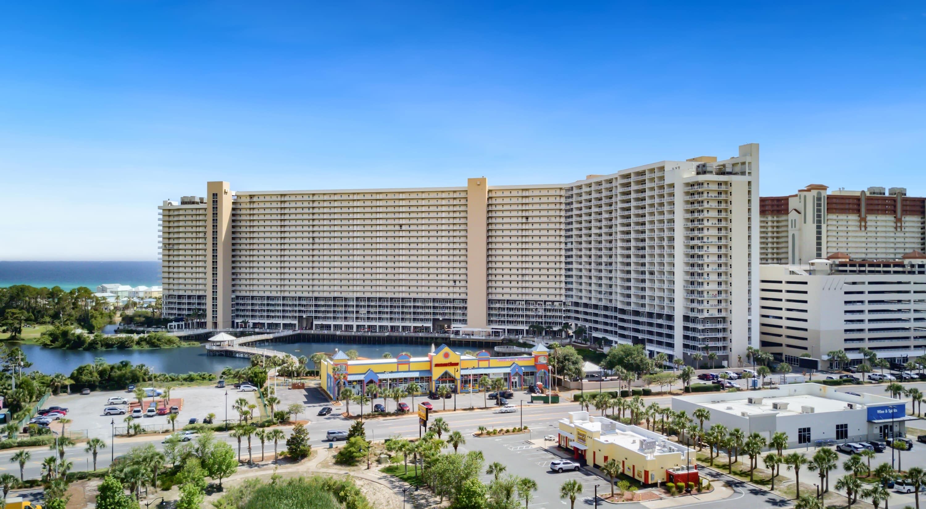 A large hotel with multiple floors, a marina, and a parking area with palm trees.