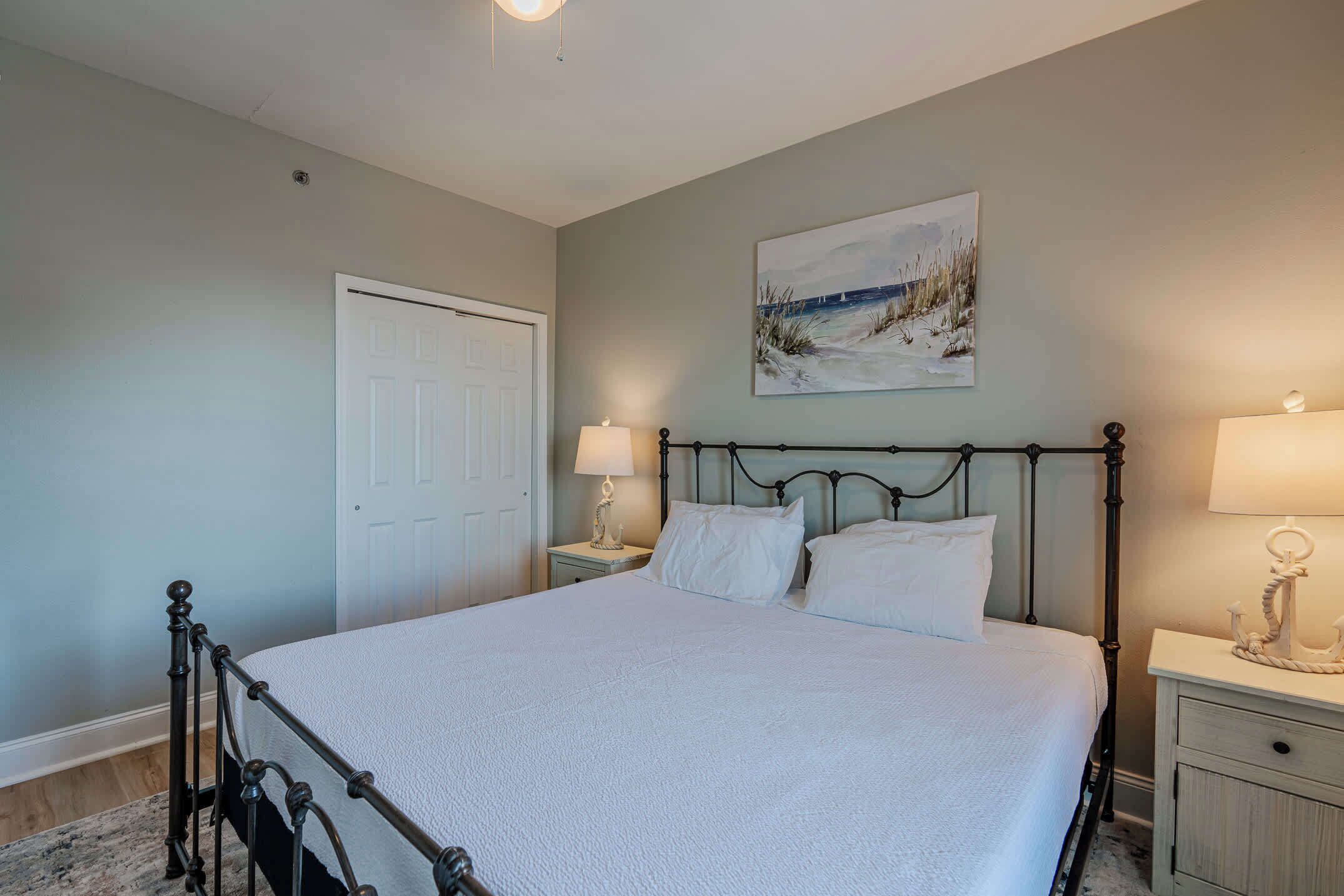 A bedroom with a bed, nightstands, a door, and a painting on the wall.