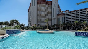 A swimming pool with a circular center, surrounded by palm trees and a large hotel building in the background. - Whitesands Retreat Incredible Resort Home! (Panama City Beach)