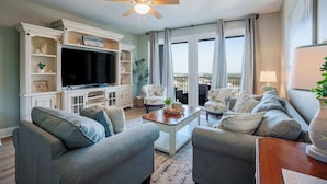 A living room with grey sofas, a coffee table, a TV, and a ceiling fan. - Whitesands Retreat Incredible Resort Home! (Panama City Beach)